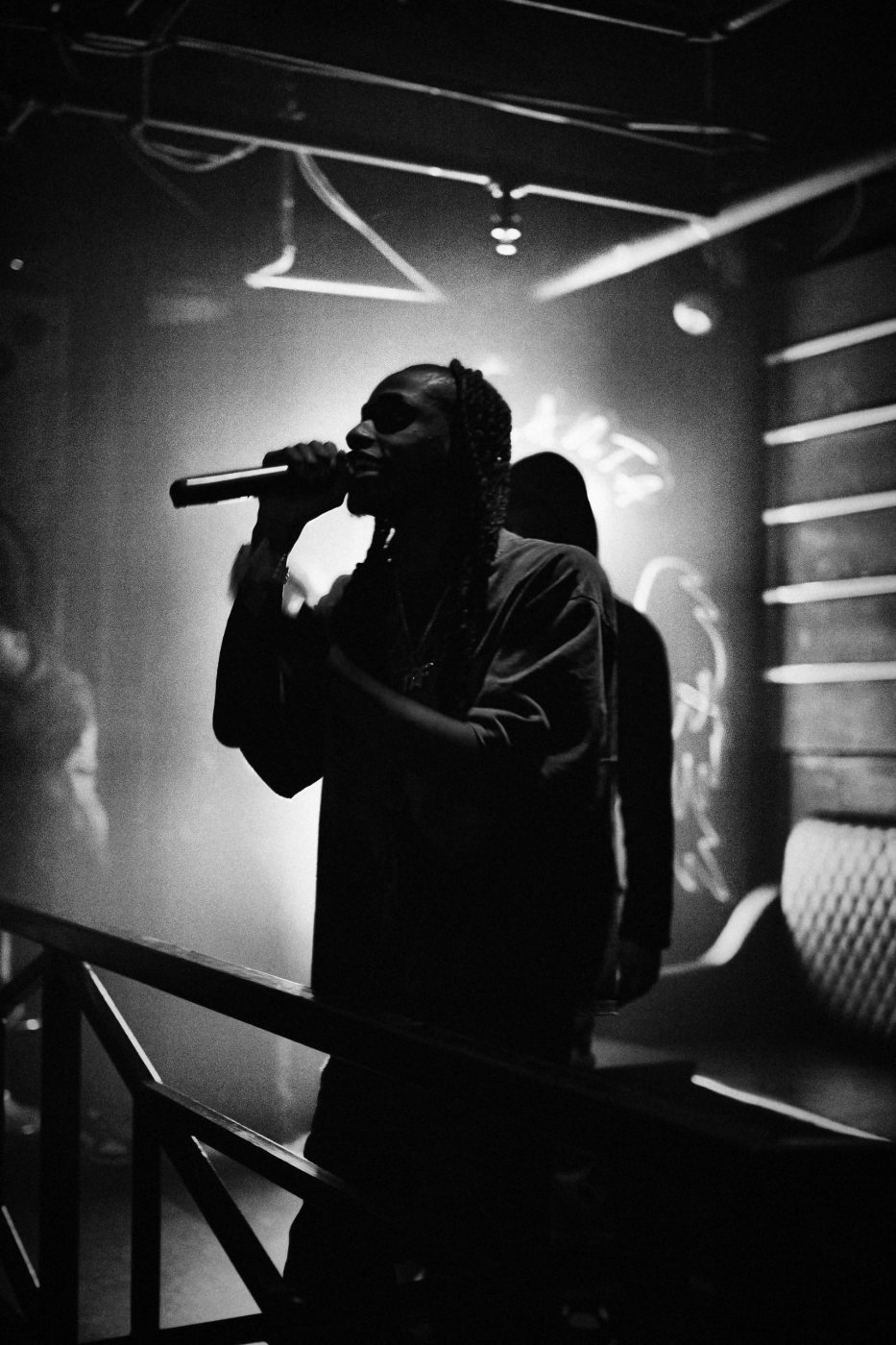 Black and white photo of TorchBinFinessin performing live, mic in hand, backlit through stage haze