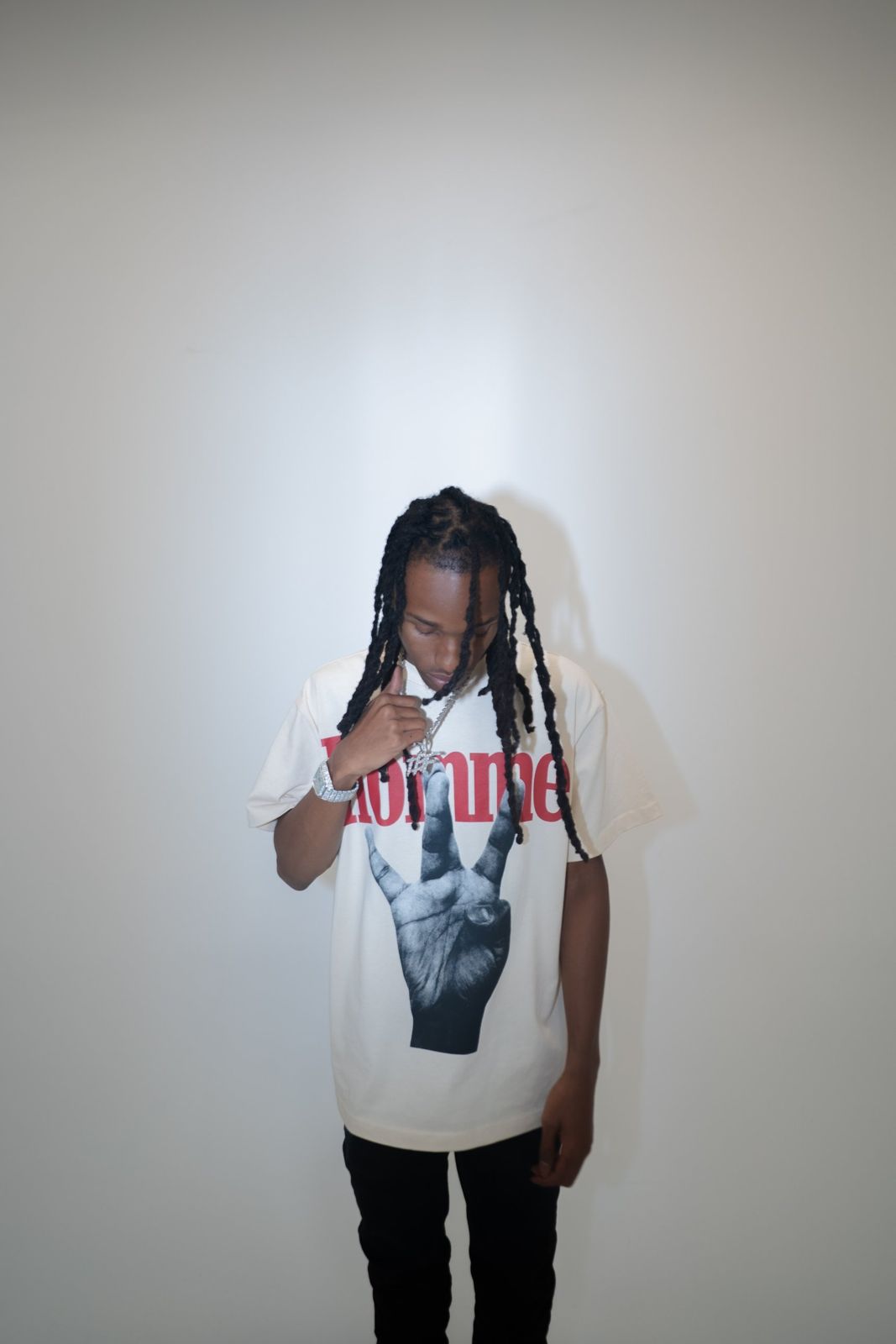 TorchBinFinessin in a cream Homme tee against a white studio wall, head down